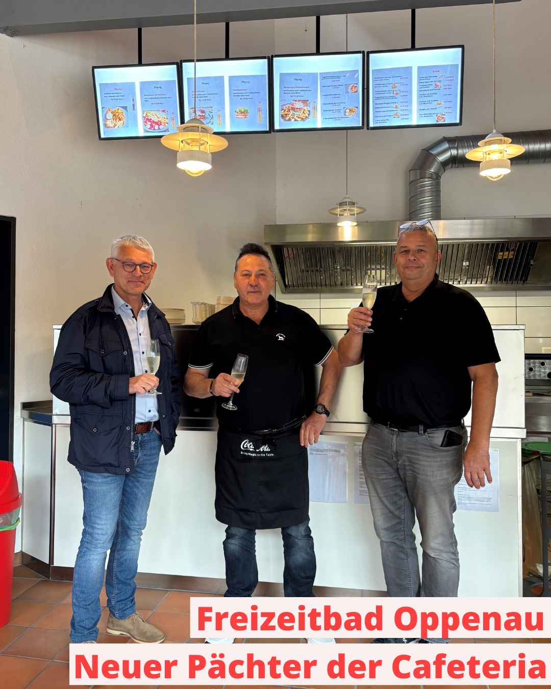 Drei Personen stehen in einer Cafeteria vor einer Theke, jede hält ein Glas Sekt. Über ihnen hängen vier digitale Menütafeln. Ein Textbanner unten besagt: „Freizeitbad Oppenau – Neuer Pächter der Cafeteria“. (KI-Alternativtext)