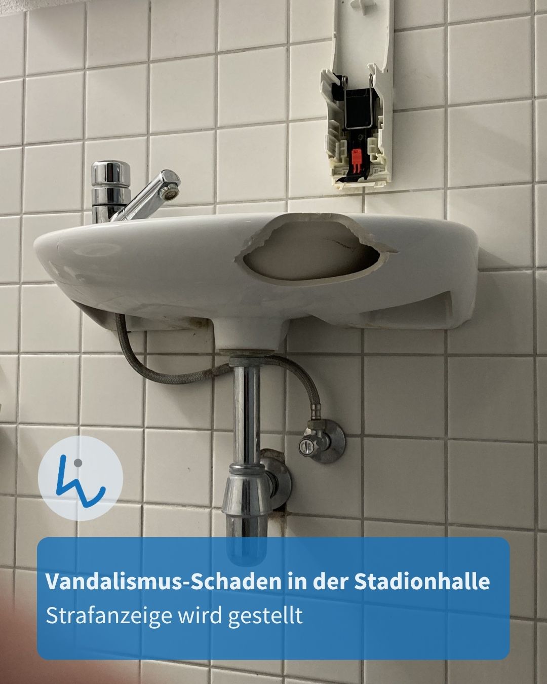 Beschädigtes Waschbecken mit großem Loch in der Keramik, montiert an einer Fliesenwand; daneben eine geöffnete, defekte Steckdose. Ein blauer Textblock unten besagt: „Vandalismus-Schaden in der Stadionhalle, Strafanzeige wird gestellt“. (KI-Alternativtext)