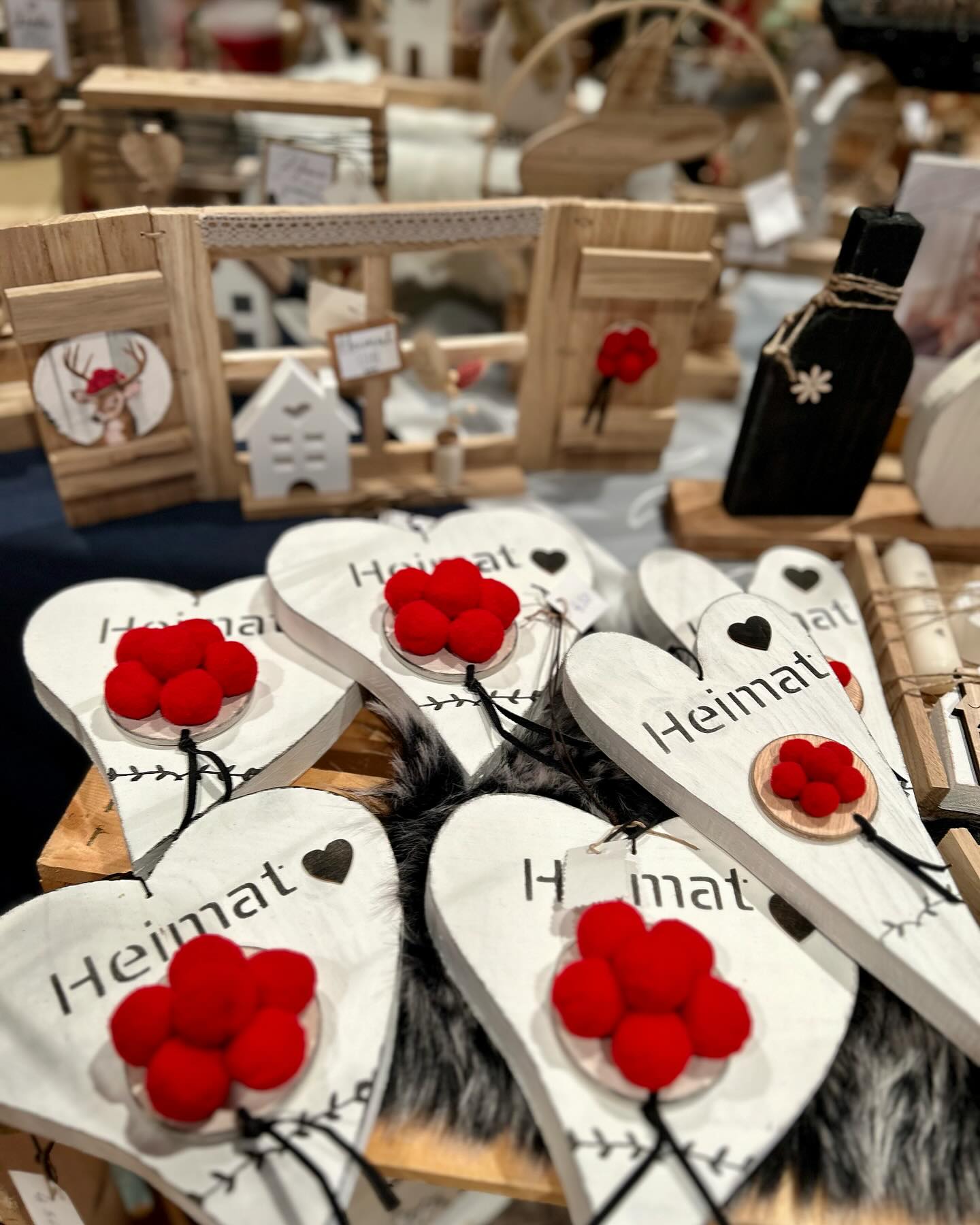 Verschiedene Dekorationsartikel, darunter weiße Holzherzen mit der Aufschrift "Heimat" und roten Verzierungen, werden präsentiert.