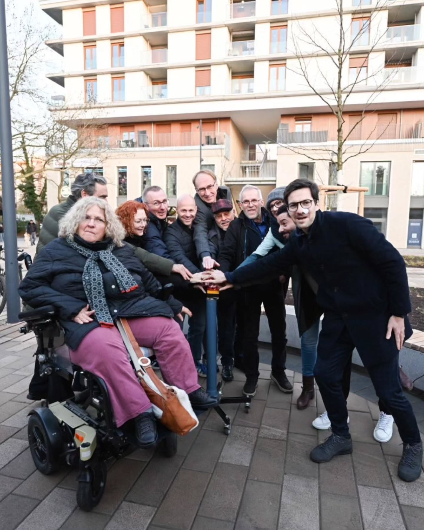 Dieser Alternativtext wurde KI-generiert: Eine Gruppe von Personen steht und sitzt im Freien vor einem modernen Gebäude. Sie scheinen ein gemeinsames Foto zu machen und zu interagieren.