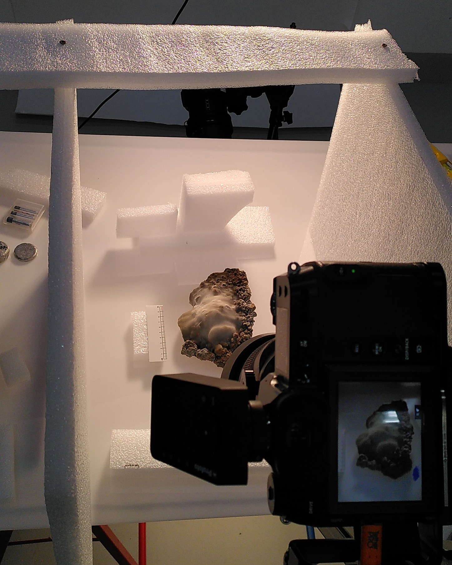 Dieser Alternativtext wurde KI-generiert: Ein Objekt, vermutlich eine Skulptur, befindet sich zwischen weißen Styroporplatten und wird von zwei Kameras aufgenommen. Auf einem Bildschirm ist das Live-Bild einer Kamera zu sehen.
