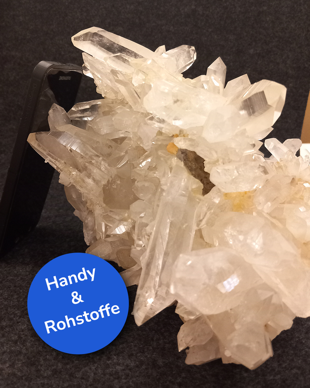 Dieser Alternativtext wurde KI-generiert: Ein Kristallhaufen steht neben einem schwarzen Objekt. Ein blaues Schild mit weißer Schrift ist im Vordergrund zu sehen.