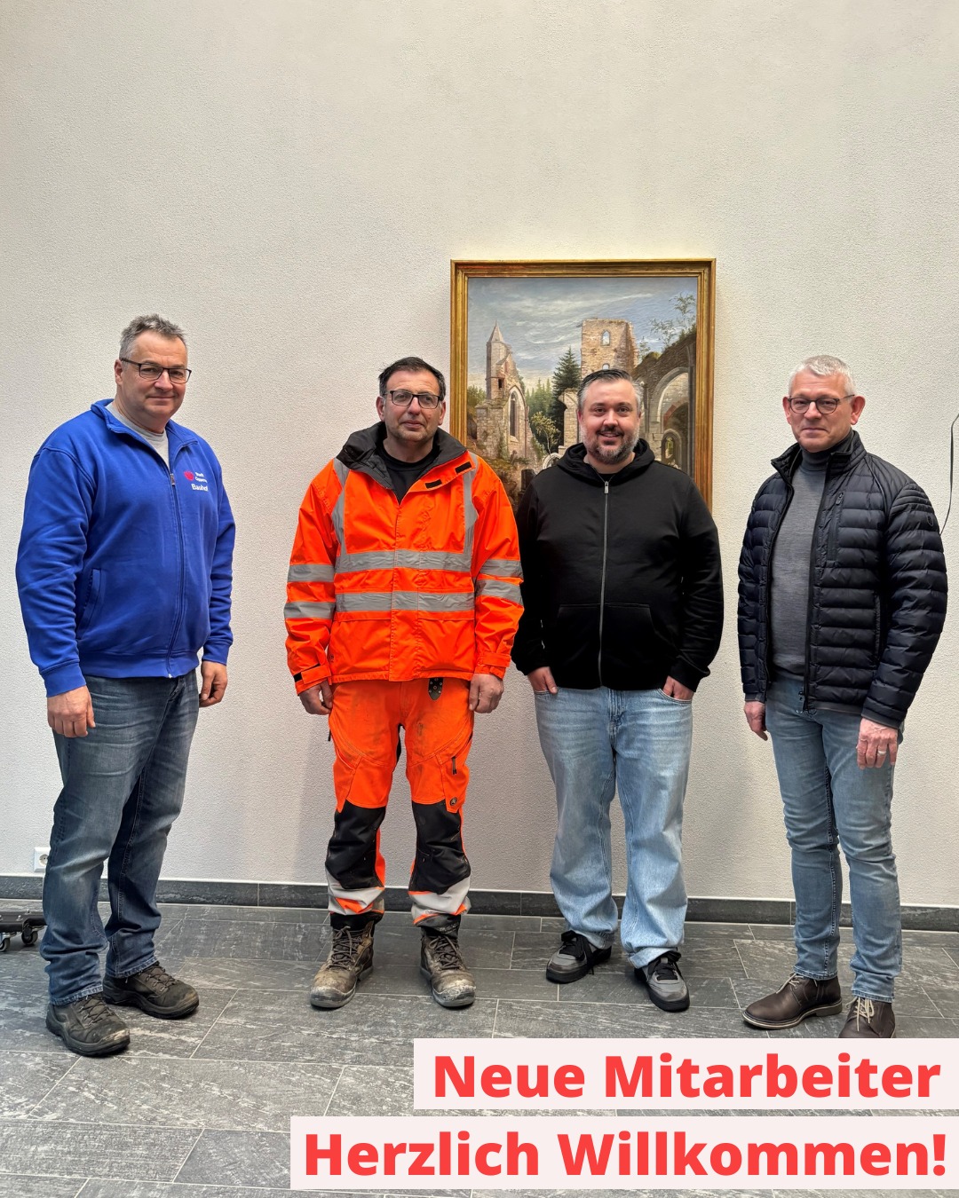 Dieser Alternativtext wurde KI-generiert: Ein farbiges Foto zeigt vier Personen, die nebeneinander vor einer Wand mit einem Gemälde stehen. Ein roter Banner mit Text befindet sich im Vordergrund.