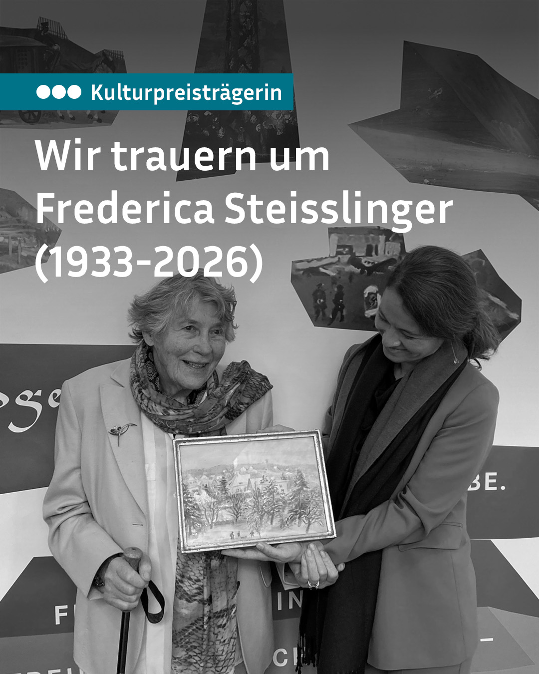 Zwei Personen stehen nebeneinander und halten gemeinsam ein gerahmtes Bild mit einer Landschaftsszene. Die Person links hält einen Gehstock und trägt einen Schal, während die Person rechts auf das Bild blickt. Oben steht der Text „Kulturpreisträgerin“ und „Wir trauern um Frederica Steisslinger (1933-2026)“. (KI-Alternativtext)