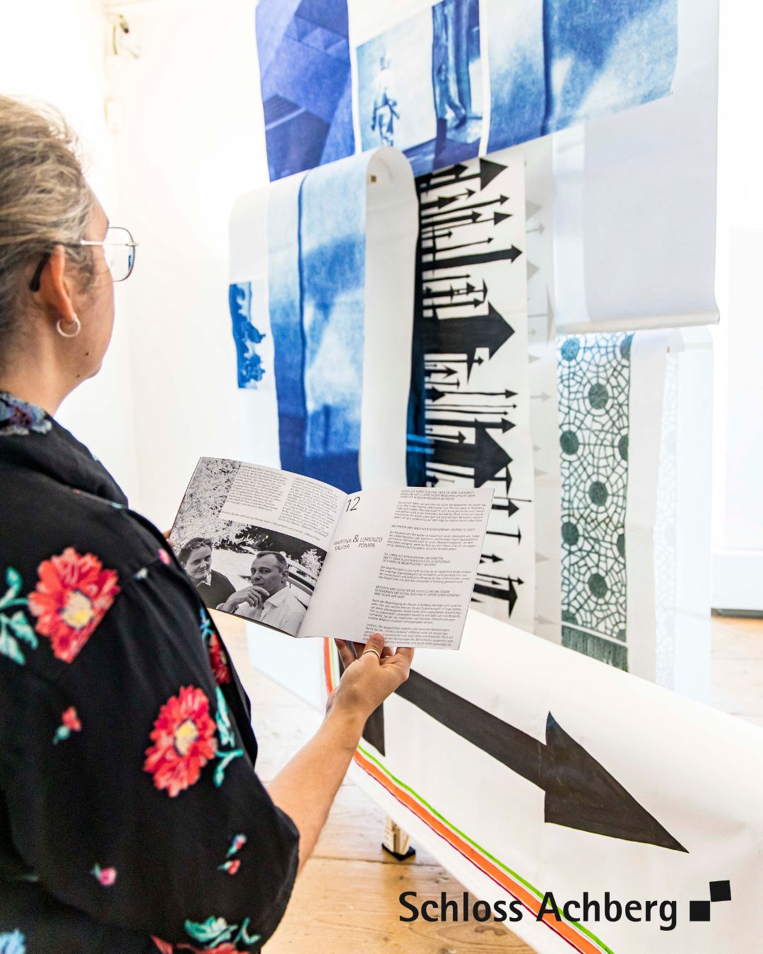 Eine Person betrachtet eine Kunstausstellung. Es sind verschiedenartige Motive auf Stoffbahnen zu sehen.