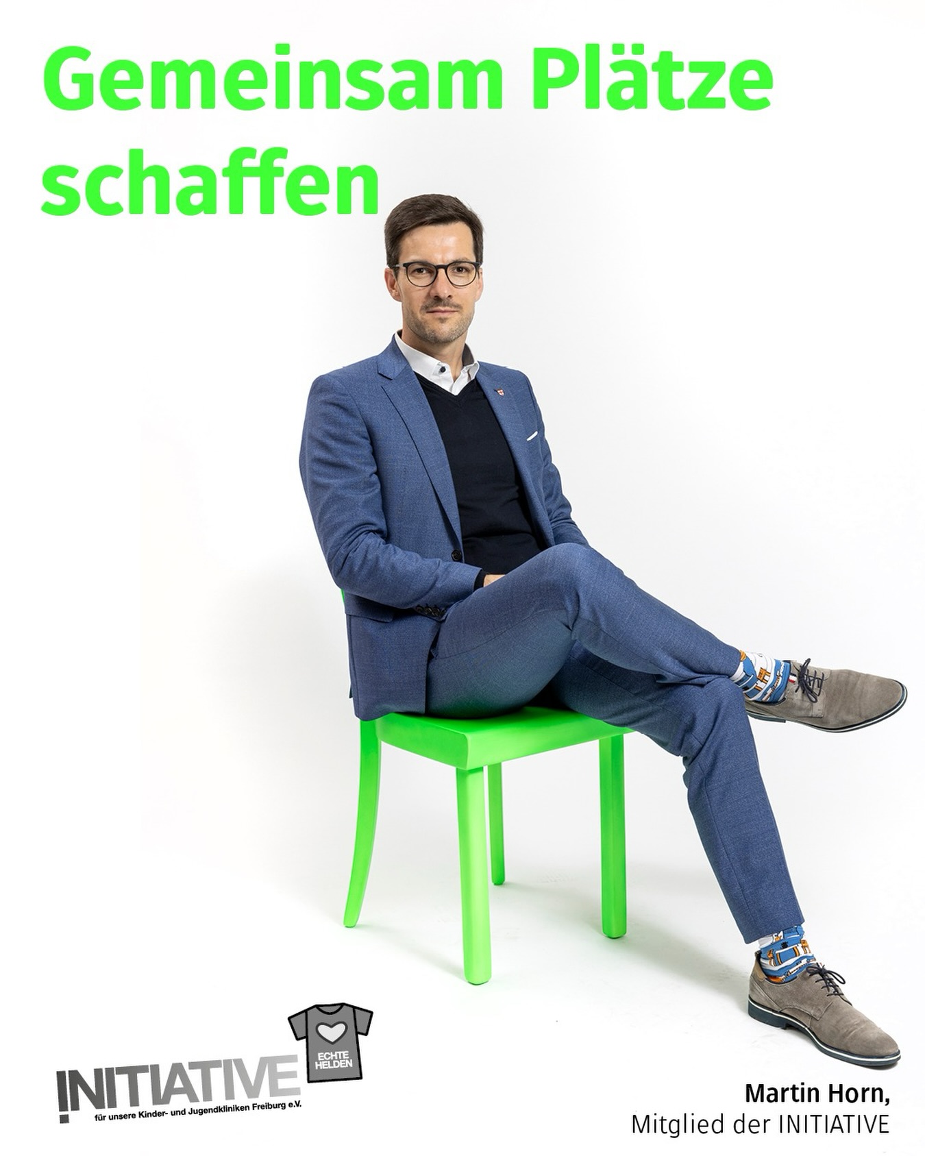 Dieser Alternativtext wurde KI-generiert: Ein Mensch in einem blauen Anzug sitzt auf einem hellgrünen Stuhl. Im Hintergrund befindet sich ein Logo und Text.