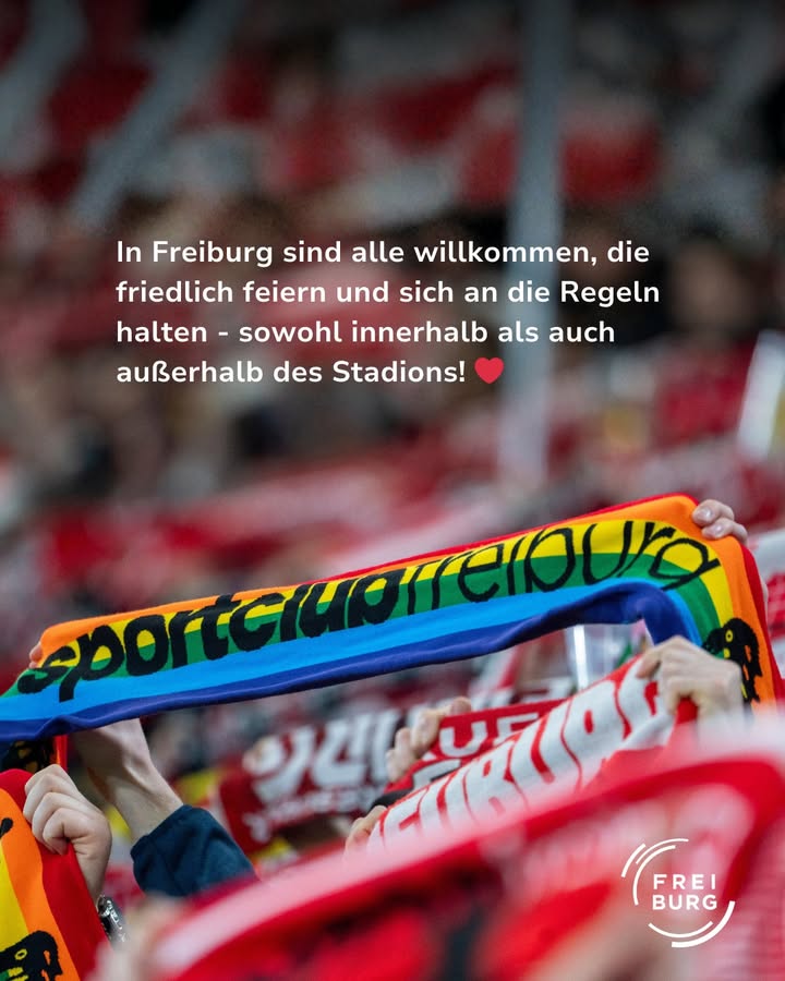 Dieser Alternativtext wurde KI-generiert: Ein unscharfer Hintergrund zeigt viele Menschen in einer Menschenmenge. Im Vordergrund ist ein Banner mit Aufschrift und die Farben einer Regenbogenflagge zu sehen.
