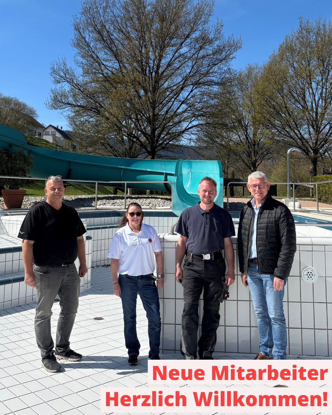 Dieser Alternativtext wurde KI-generiert: Drei Personen stehen vor einem Schwimmbecken und einer Wasserrutsche. Im Vordergrund befindet sich ein rotes Banner mit einem Begrüßungstext.