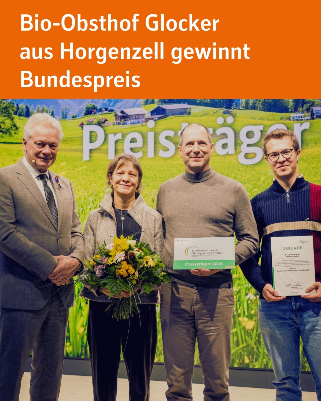 Zu sehen sind vier Personen, die nebeneinander auf einer Bühne stehen. Drei davon sind Preisträger und halten Blumen sowie Urkunden in der Hand und blicken in die Kamera.
Bildtext: Bio-Obsthof Glocker
aus Horgenzell gewinnt Bundespreis