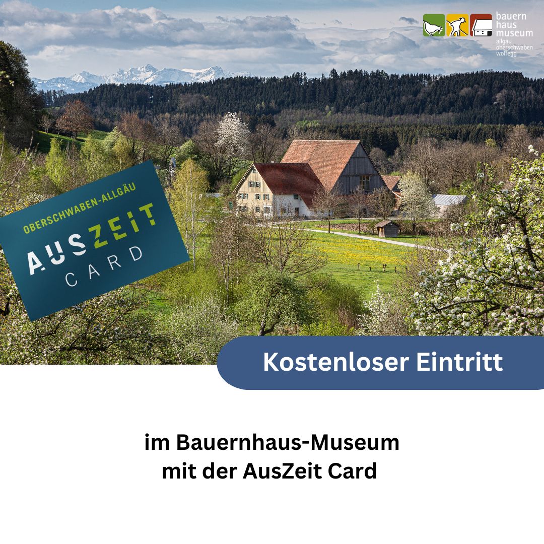 Dieser Alternativtext wurde KI-generiert: Ein traditionelles Bauernhaus mit rotem Dach steht vor einer Hügellandschaft. Im Vordergrund befindet sich ein blaues Schild mit Text und Logo.