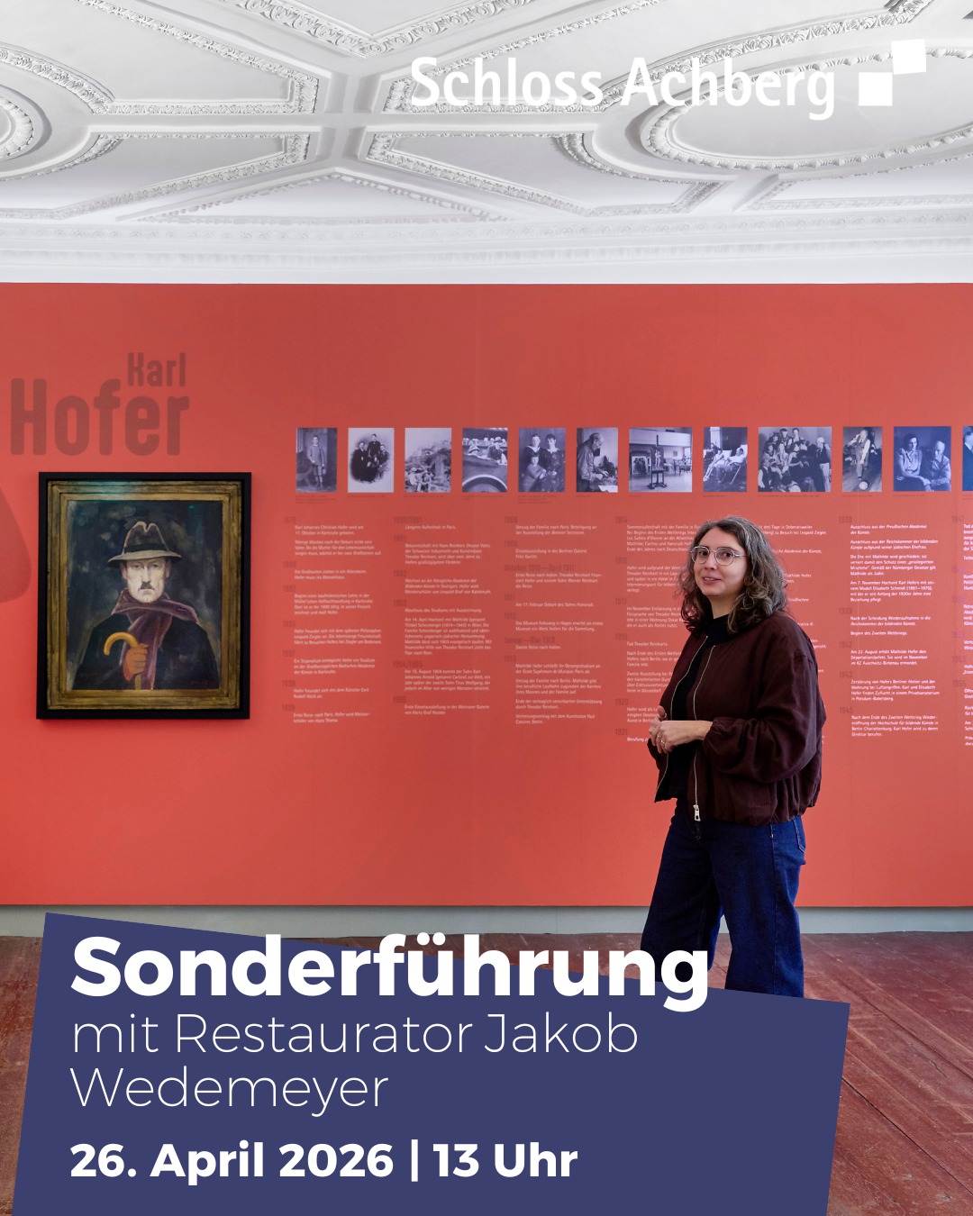 Dieser Alternativtext wurde KI-generiert: Ein Innenraum mit roten Wänden und einer Stuckdecke. An den Wänden hängen Bilder und Informationstafeln, eine Person steht davor und betrachtet diese.