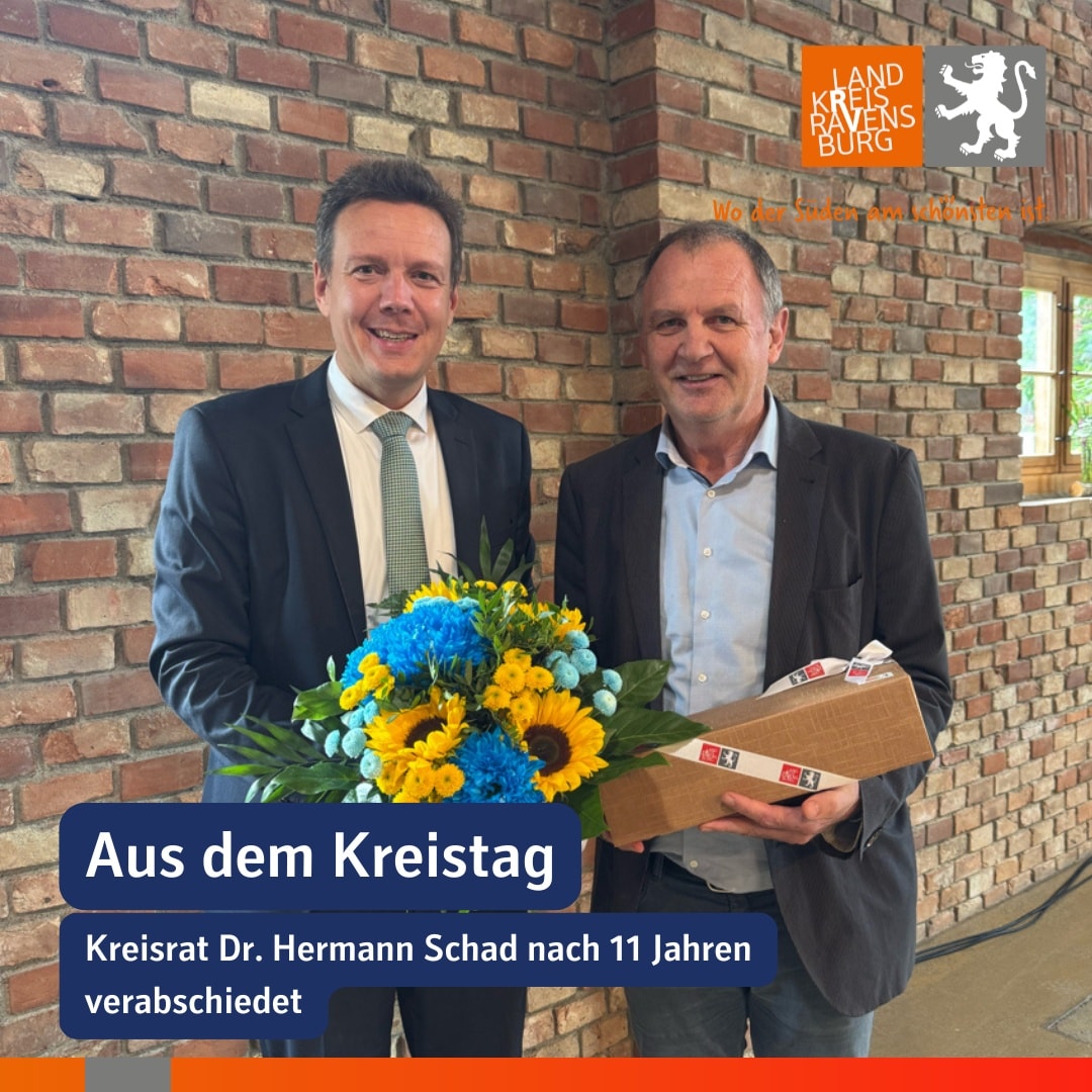 Zwei Personen stehen vor einer Ziegelwand. Eine Person hält einen Blumenstrauß, die andere eine Schachtel.