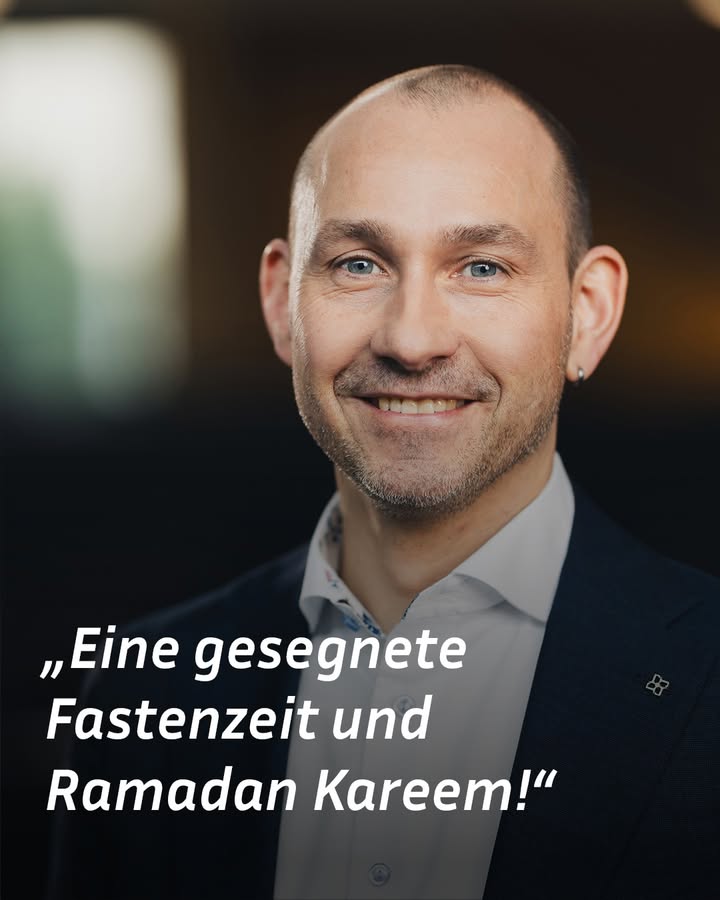 Dieser Alternativtext wurde KI-generiert: Porträt einer lächelnden Person mit hellem Hemd und dunklem Blazer. Im Vordergrund steht ein Text in deutscher Sprache, der "Eine gesegnete Fastenzeit und Ramadan Kareem!" wünscht.