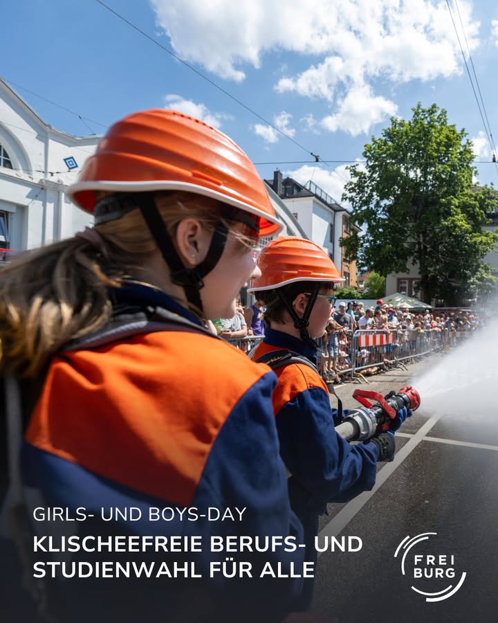 Zwei Personen in orangenen Helmen halten einen Feuerwehrschlauch.  Dies ist ein Bild vom Girls- und Boys-Day.