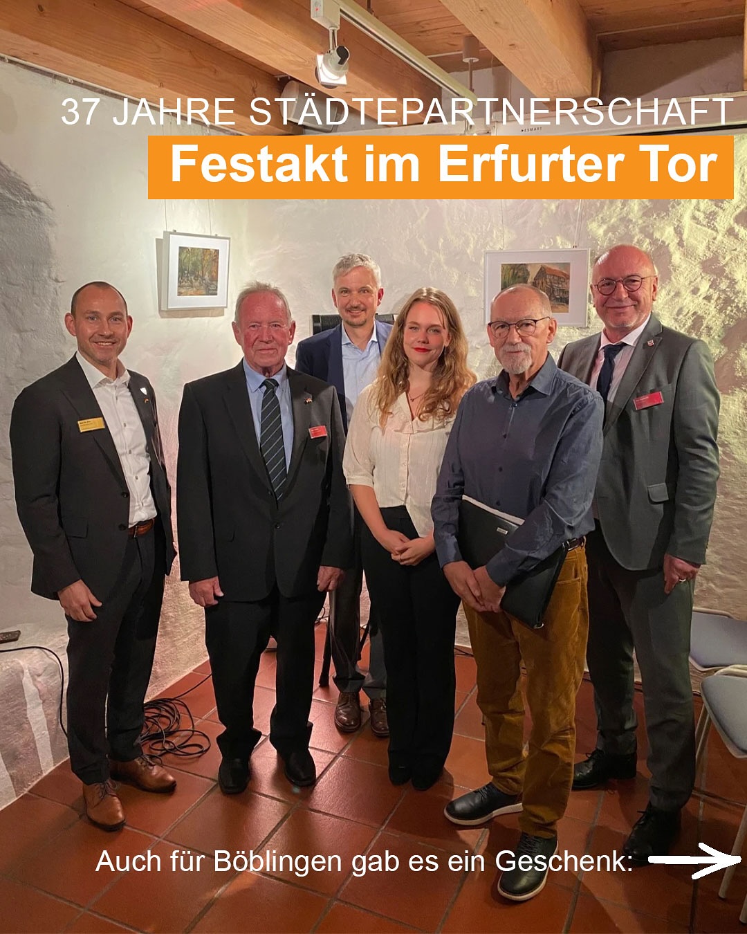 Dieser Alternativtext wurde KI-generiert: Ein Gruppenfoto von mehreren Personen in formeller Kleidung steht vor einer steinernen Wand. Im Hintergrund befinden sich gerahmte Bilder.