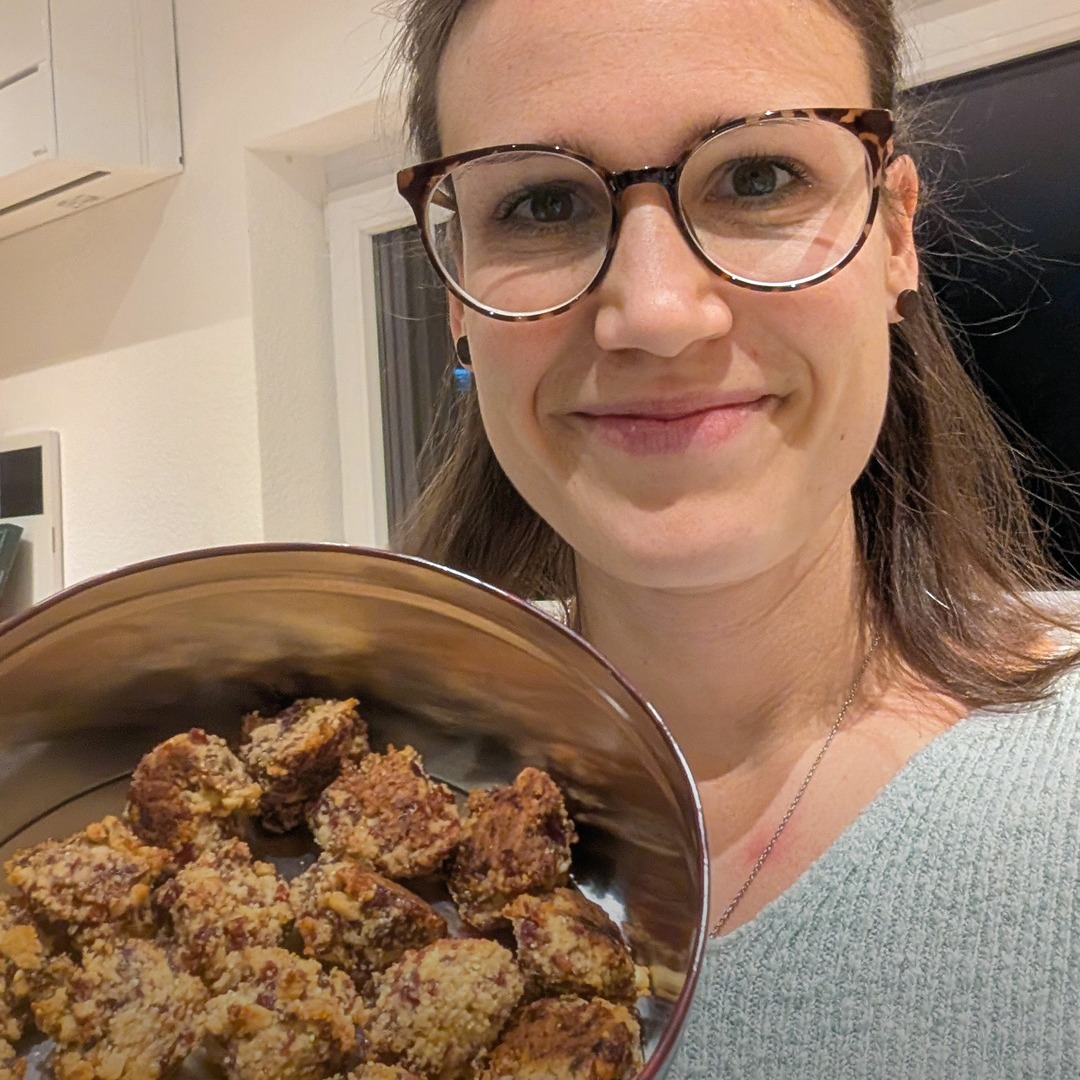 Dieser Alternativtext wurde KI-generiert: Eine Person hält eine Schüssel mit kleinen, braunen Leckereien vor sich. Im Hintergrund ist eine Küche zu sehen.