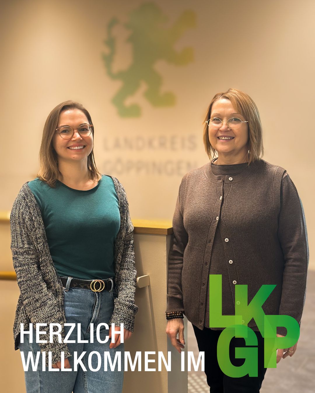 Dieser Alternativtext wurde KI-generiert: Zwei Personen stehen nebeneinander vor einem Hintergrund mit einem Logo und Text. Im Vordergrund befindet sich ein Willkommensgruß.