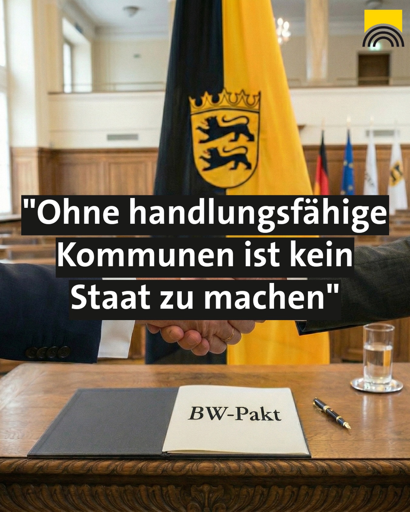 Dieser Alternativtext wurde KI-generiert: Ein Innenraum mit Tischen und Stühlen. Im Vordergrund eine Person, die einen Dokumentenordner hält, vor einer Flagge und einem Schild mit Text.