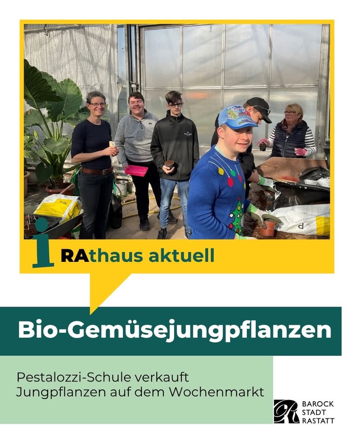 Dieser Alternativtext wurde KI-generiert: Eine Gruppe von Personen steht in einem Gewächshaus vor Pflanzen und Tischen mit Waren. Im Vordergrund befinden sich Schilder mit Informationen zu Gemüsejungpflanzen und einem Wochenmarkt.