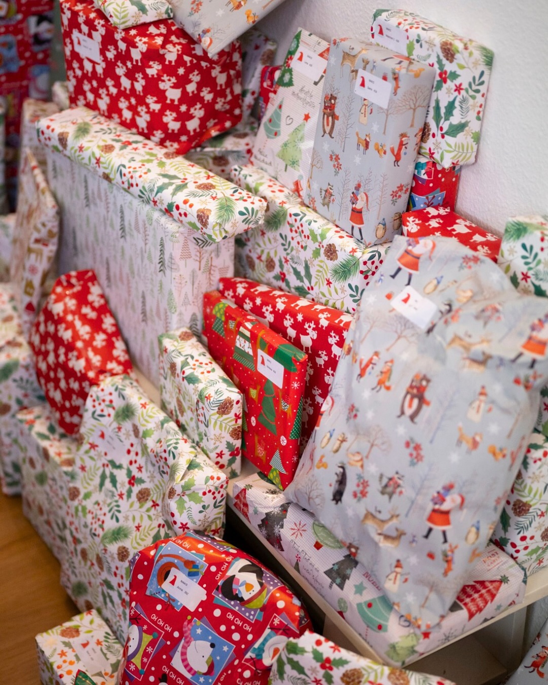 Dieser Alternativtext wurde KI-generiert: Ein Haufen bunt verpackter Geschenke bedeckt einen Sessel und andere Oberflächen. Die Geschenkverpackungen haben verschiedene weihnachtliche Motive und Muster.