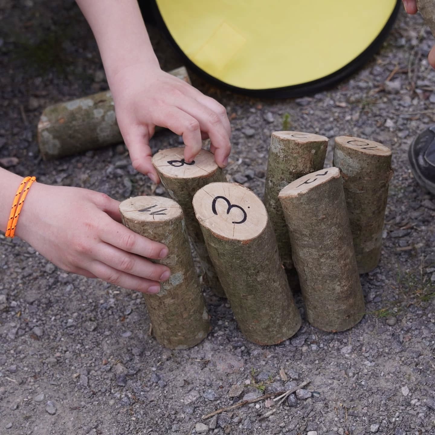 Kinderhände arrangieren Holzklötze mit Zahlen darauf auf dem Boden. Ein gelber Gegenstand liegt im Hintergrund.