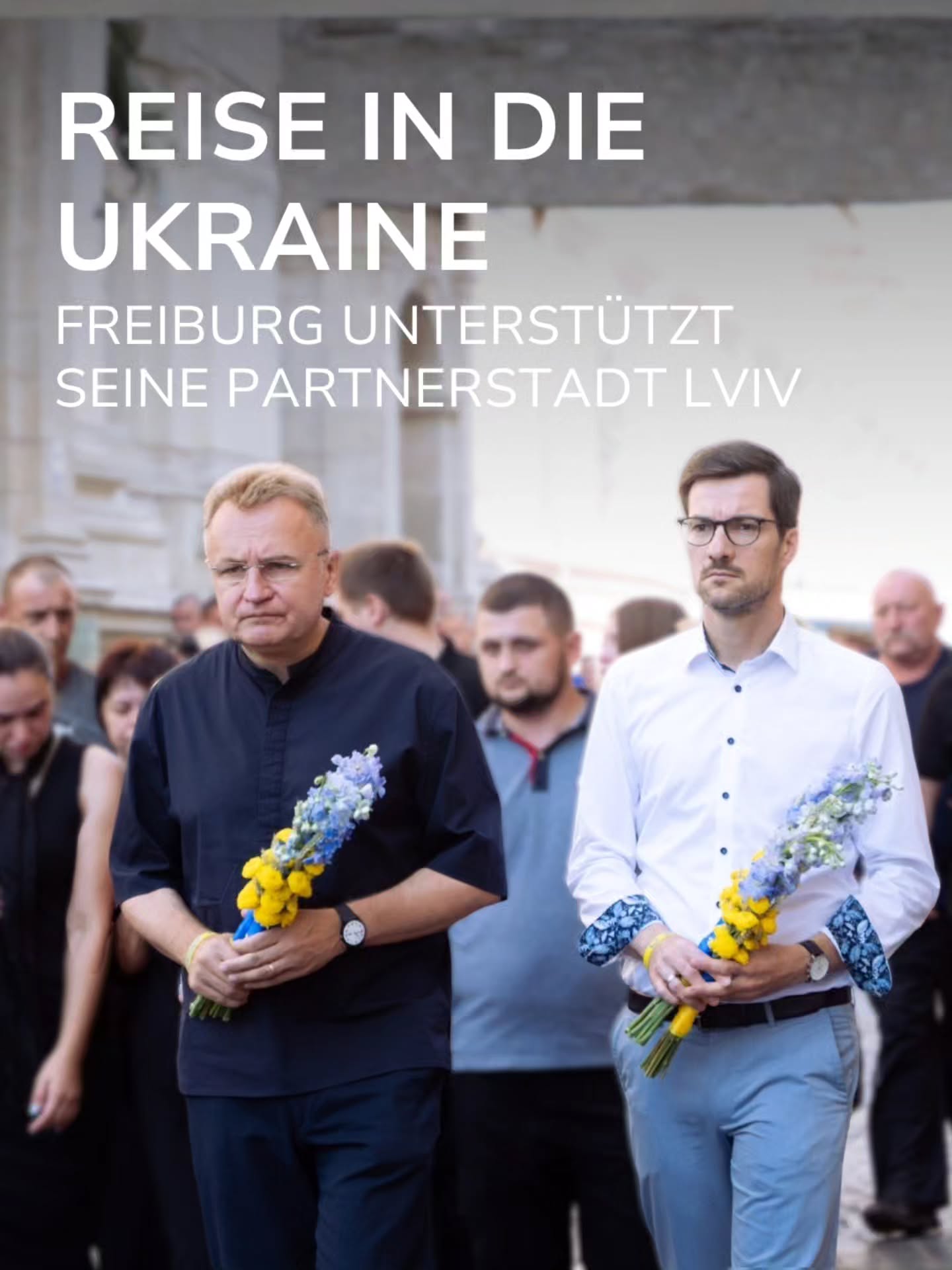 Zwei Personen gehen im Vordergrund nebeneinander und halten Sträuße mit blauen und gelben Blumen. Oben steht der Text: REISE IN DIE UKRAINE. FREIBURG UNTERSTÜTZT SEINE PARTNERSTADT LVIV. Im Hintergrund sind weitere Personen unscharf zu erkennen. (KI-Alternativtext)