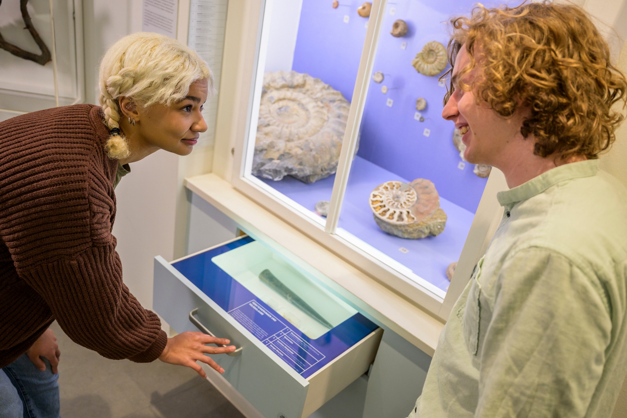 Dieser Alternativtext wurde KI-generiert: Zwei Personen betrachten gemeinsam eine Vitrine mit Objekten darin. Die Ausstellung scheint sich mit Naturgeschichte oder einem ähnlichen Thema zu befassen.