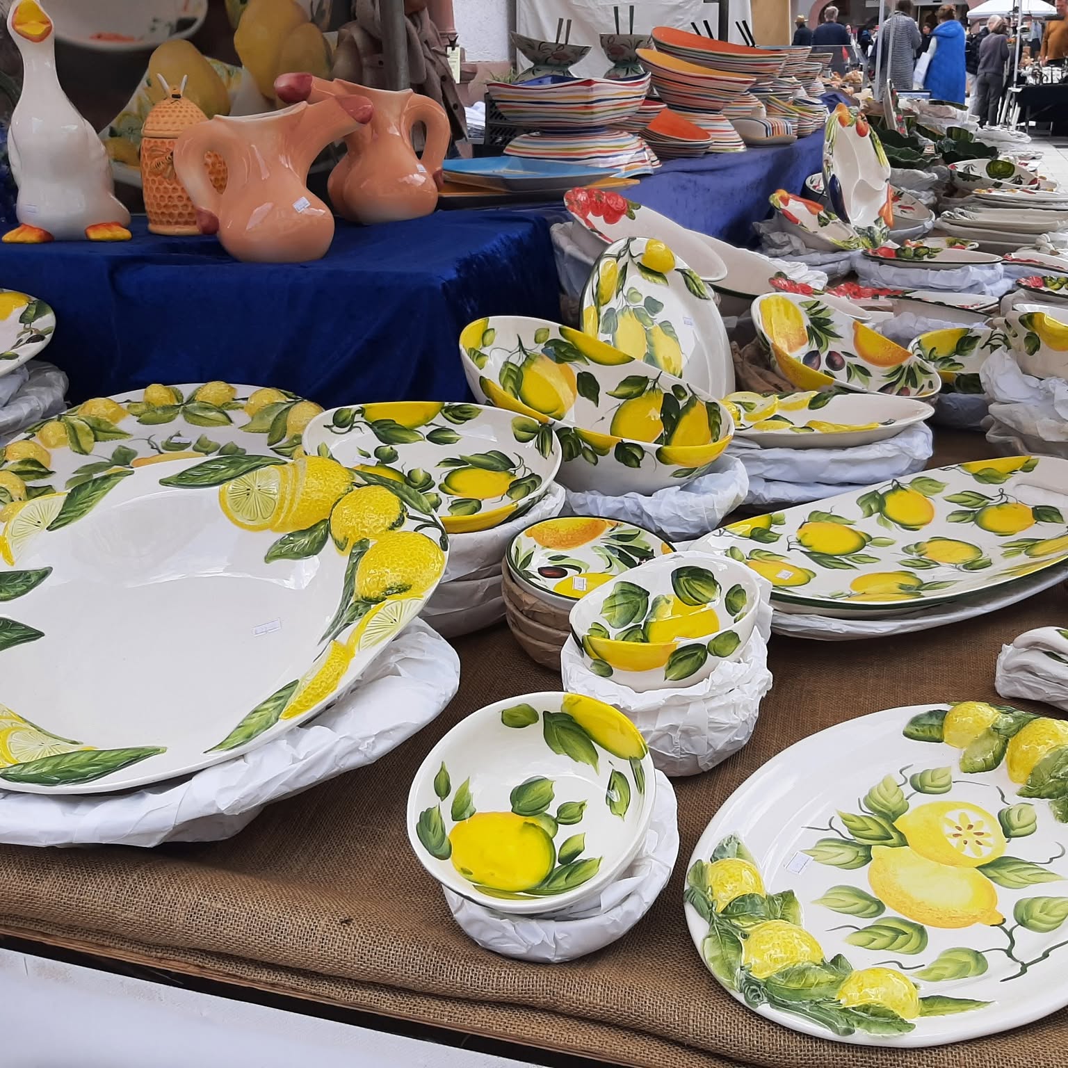Handbemalte Keramikgeschirr mit Zitronenmotiv auf einem Marktstand. Verschiedene Schalen, Teller und Servierplatten sind zu sehen.