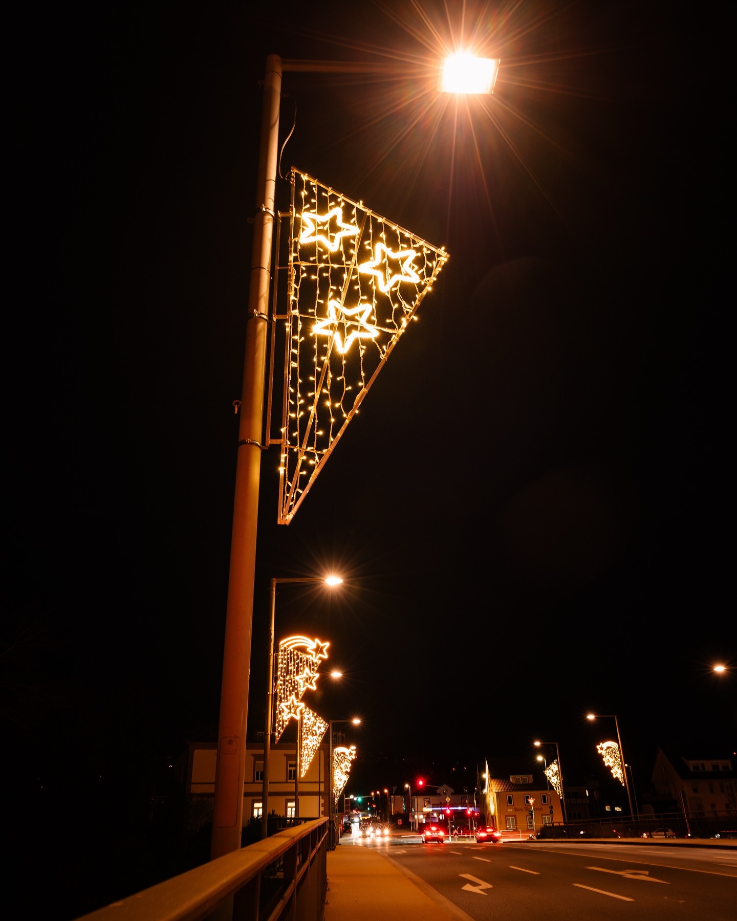 Beleuchtete Straßenlaternen mit festlicher Dekoration schmücken eine nächtliche Straße. Die Lichter erzeugen eine warme und gemütliche Atmosphäre.