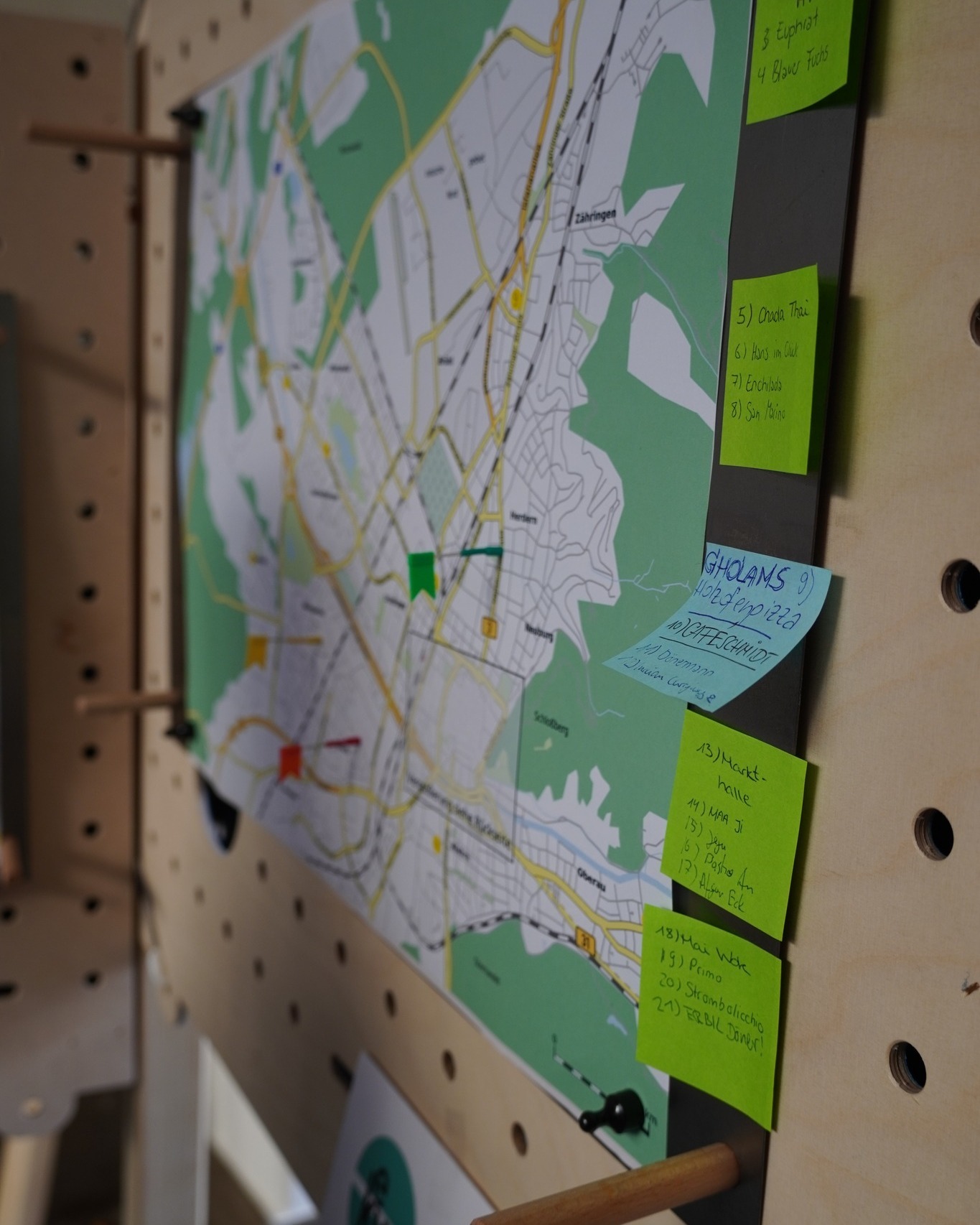 Dieser Alternativtext wurde KI-generiert: Eine Karte mit Markierungen und Notizen hängt an einer Lochwand. Verschiedene Orte sind mit Haftnotizen versehen, auf denen Text geschrieben steht.