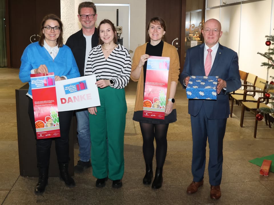 Dieser Alternativtext wurde KI-generiert: Mehrere Personen stehen nebeneinander und halten Informationsmaterial in den Händen. Im Hintergrund befindet sich eine weihnachtliche Dekoration.