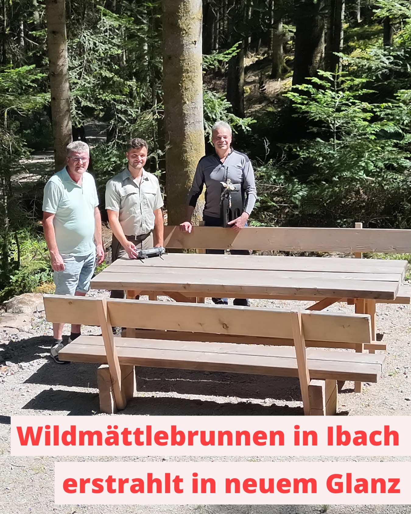 Drei Personen stehen im Wald hinter einem neuen Holztisch mit Bänken, wobei eine Person eine Nagelklammer auf der Tischplatte hält und eine andere ein Holzbrett stützt. Ein Textfeld unten lautet: „Wildmättlebrunnen in Ibach erstrahlt in neuem Glanz“. (KI-Alternativtext)