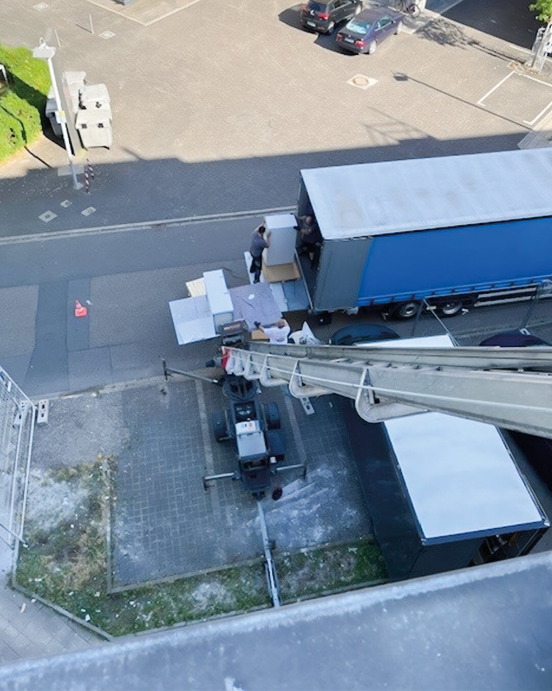 Dieser Alternativtext wurde KI-generiert: Eine Aufnahme von oben zeigt einen Umzug. Gegenstände werden von einem LKW abgeladen, während Personen dabei helfen.