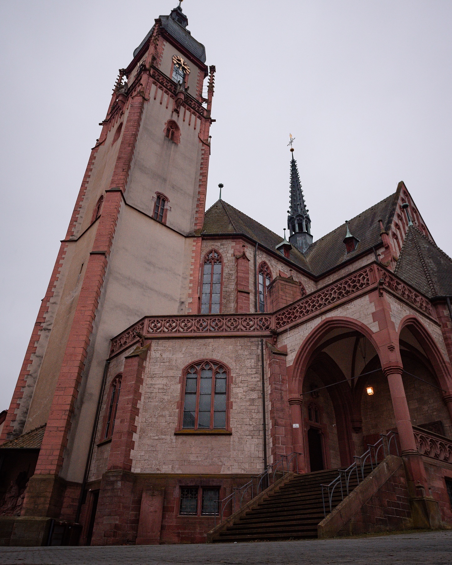 Eine alte Kirche mit hohem Turm und Steintreppe. Das Gebäude ist aus Stein und Ziegeln gebaut und wirkt sehr imposant.