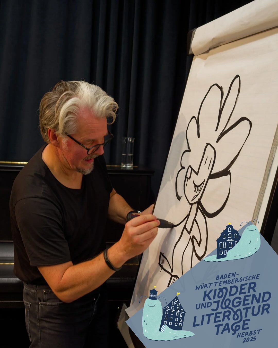 Dieser Alternativtext wurde KI-generiert: Ein Mann zeichnet mit einem Stift auf ein großes Papier. Im Hintergrund ist ein Banner mit Text und Illustrationen zu sehen.