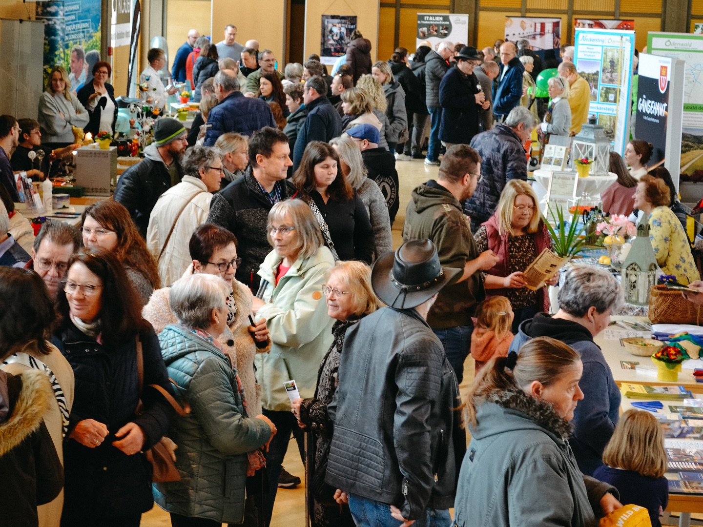 Viele Menschen stehen dicht gedrängt auf einer Messe oder einem Markt. Es gibt Stände mit Informationsmaterial und Pflanzen.