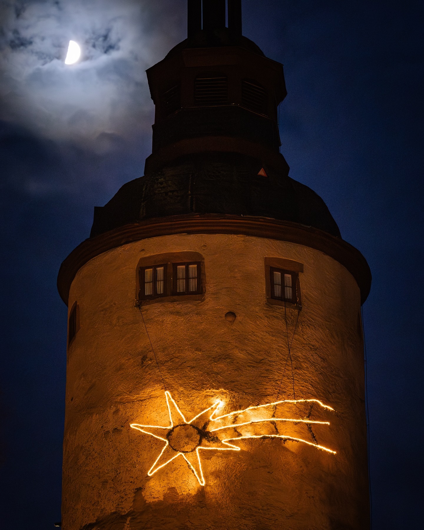 Ein runder Turm bei Nacht mit einem leuchtenden Stern und Schweif. Der Halbmond ist am Himmel zu sehen.