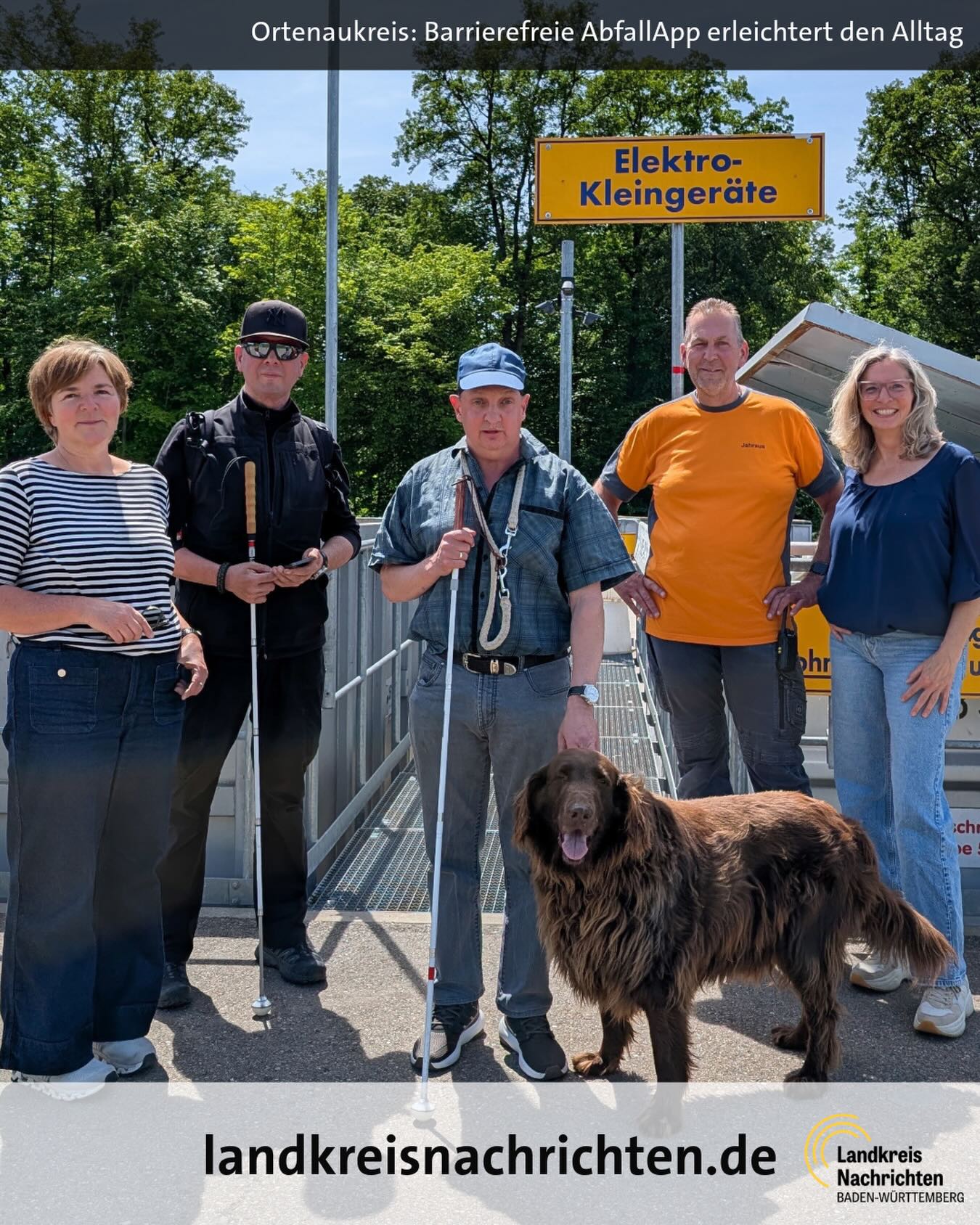 Fünf Personen und ein brauner Hund stehen vor einem Schild mit der Aufschrift „Elektro-Kleingeräte“. Zwei Personen halten weiße Blindenstäbe, eine hat einen Blindenhund an der Leine. Im Hintergrund sind Bäume und ein Recyclinghof zu sehen. (KI-Alternativtext)