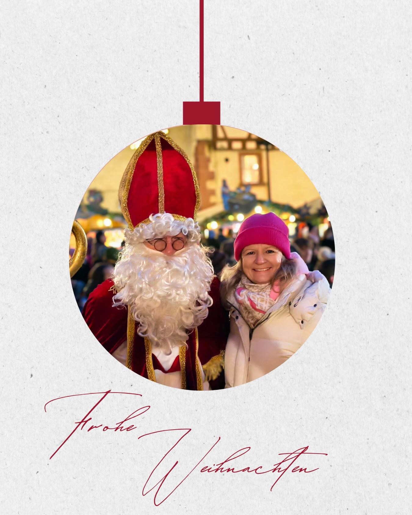 Dieser Alternativtext wurde KI-generiert: Ein farbiges Bild zeigt eine weihnachtliche Szene mit einer Person in traditioneller Verkleidung und einer weiteren Person, die in die Kamera lächelt. Im Hintergrund ist ein beleuchteter Weihnachtsmarkt zu sehen.