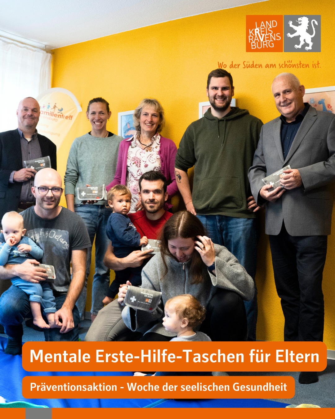 Dieser Alternativtext wurde KI-generiert: Eine farbenfrohe Aufnahme zeigt eine Gruppe von Personen, die zusammen posieren. Im Vordergrund sind Schilder und Werbematerialien mit dem Hinweis auf psychische Erste Hilfe für Eltern zu sehen.