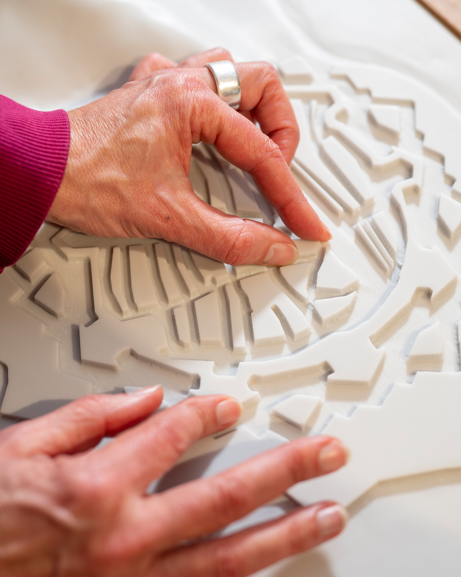 Dieser Alternativtext wurde KI-generiert: Hände untersuchen ein strukturiertes, weißes Objekt. Das Bild ist farbig und zeigt Nahaufnahme von Textur und Geste.