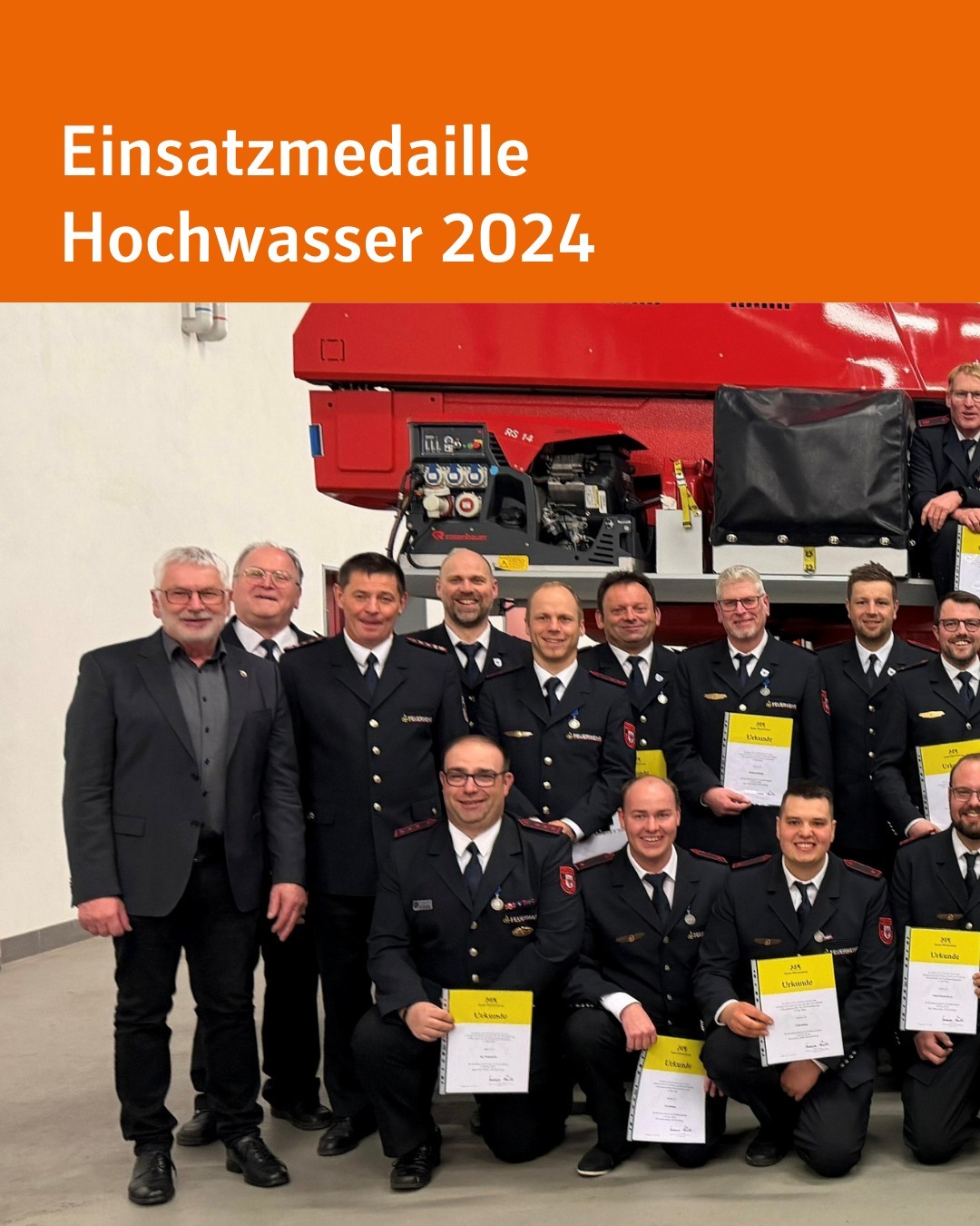 Linke Hälfte eines Fotos mit Menschen in Feuerwehruniformen, nebeneinander gereiht und mit Urkunden in den Händen. Sie stehen vor einem Feuerwehrfahrzeug. Text im Bild: Einsatzmedaille Hochwasser 2024