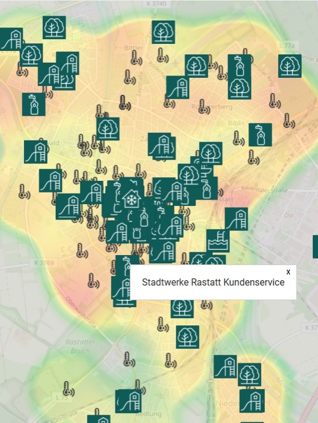 Karte von Rastatt mit grünen Symbolen für Gebäude, Bäume und Wasser sowie Thermometer-Symbolen. Ein Pop-up zeigt „Stadtwerke Rastatt Kundenservice“. Hintergrundfarben deuten Temperaturverteilung an. (KI-Alternativtext)