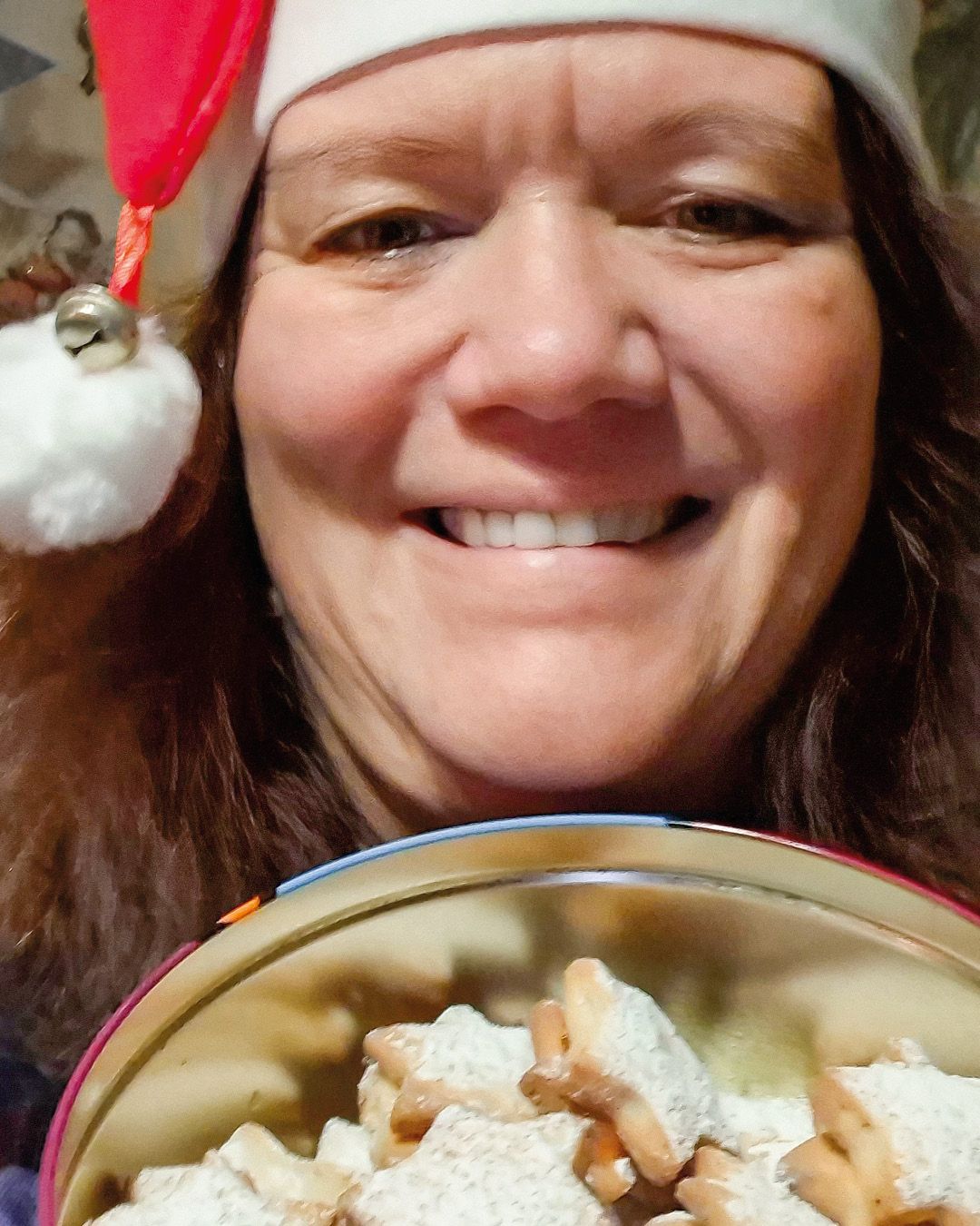 Dieser Alternativtext wurde KI-generiert: Eine Person lächelt in die Kamera. Im Vordergrund ist ein Teller mit hellen, gebackenen Leckereien zu sehen.