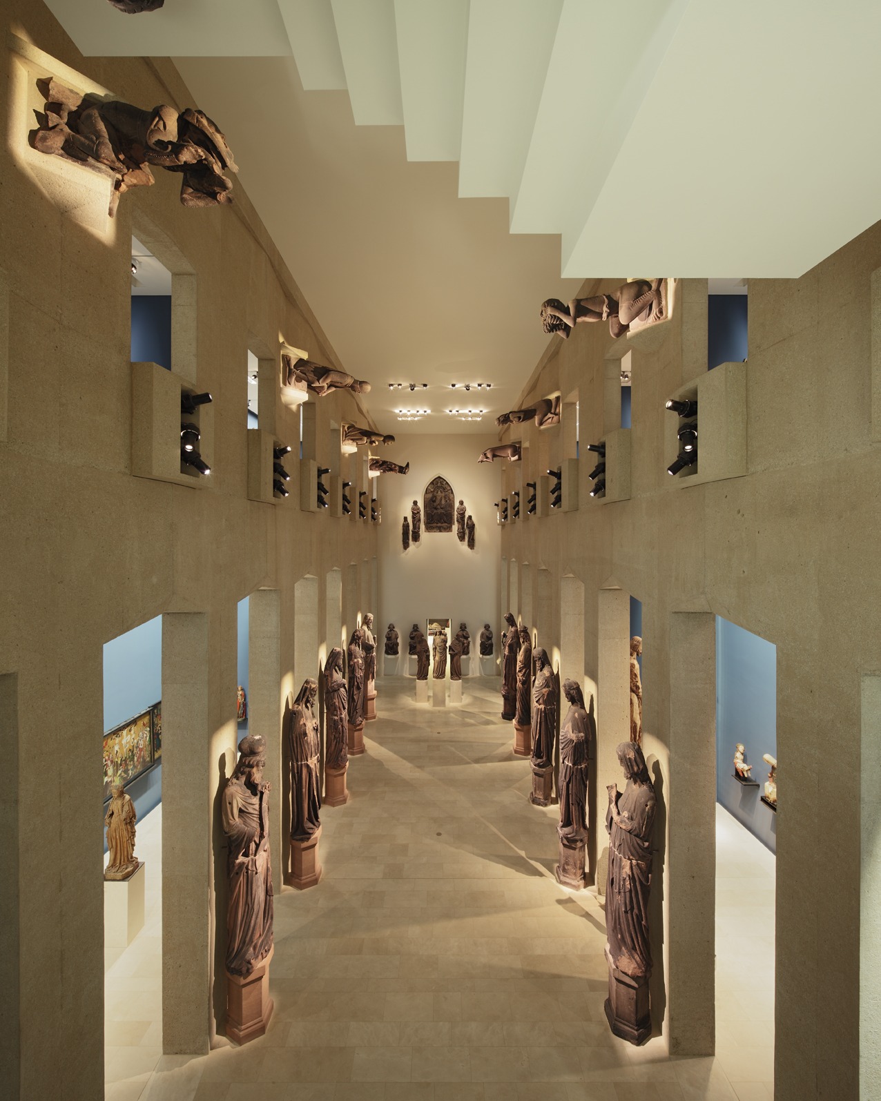 Dieser Alternativtext wurde KI-generiert: Ein Innenraum mit Architektur in hellen Farbtönen. Statuen sind entlang einer zentralen Achse und in Nischen angeordnet.