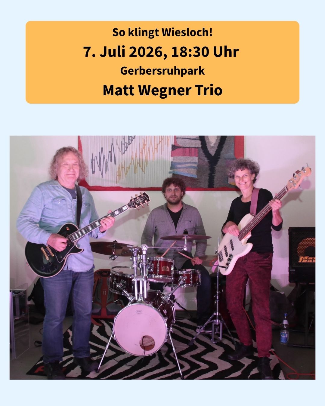 Konzertplakat mit dem Text "So klingt Wiesloch! 7. Juli 2026, 18:30 Uhr Gerbersruhpark Matt Wegner Trio". Darunter ein Foto von drei Musikern: links eine Person mit schwarzer E-Gitarre, in der Mitte eine Person am Schlagzeug und rechts eine Person mit weißem Bass. (KI-Alternativtext)