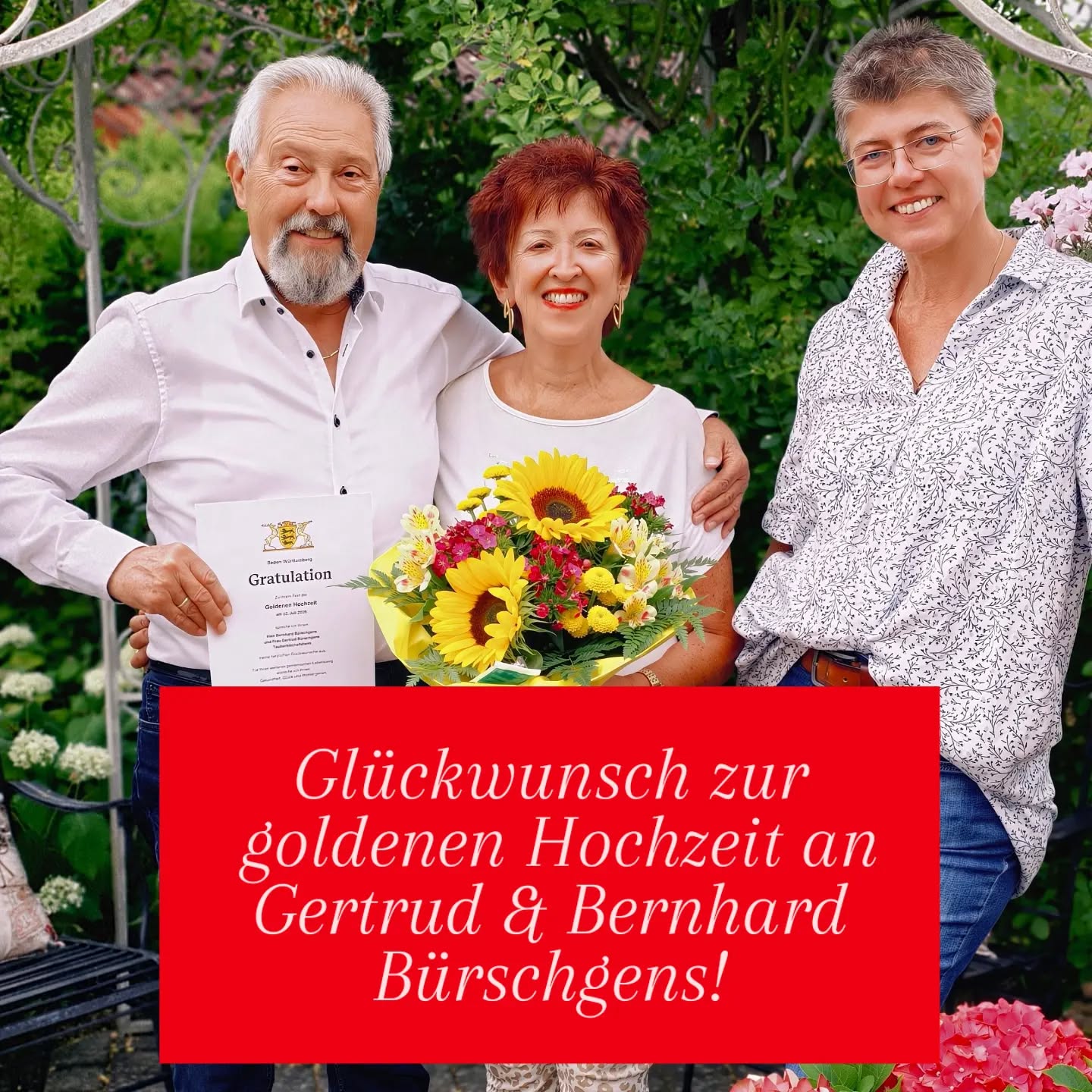 Drei Personen stehen lächelnd im Freien nebeneinander. Die Person links hält ein Zertifikat mit der Aufschrift „Gratulation“ und „Guldener Hochzeit“, während die Person in der Mitte einen Blumenstrauß mit Sonnenblumen hält. Ein roter Textblock am unteren Bildrand lautet: „Glückwunsch zur goldenen Hochzeit an Gertrud & Bernhard Bürschgens!“ (KI-Alternativtext)