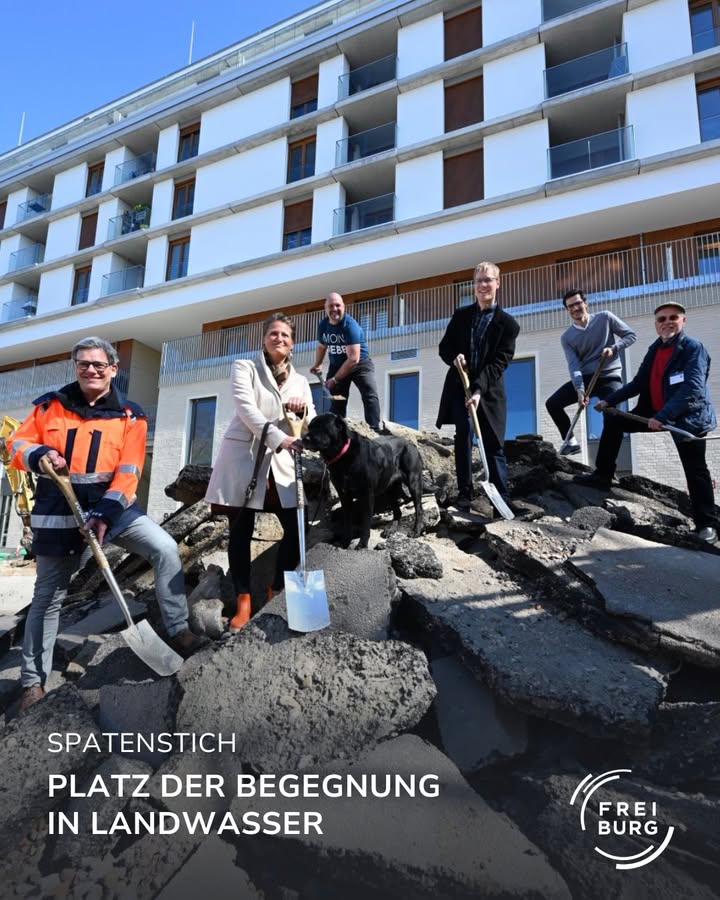 Gruppe von Menschen mit Spaten vor einem Gebäude. Spatenstich für ein neues Projekt.