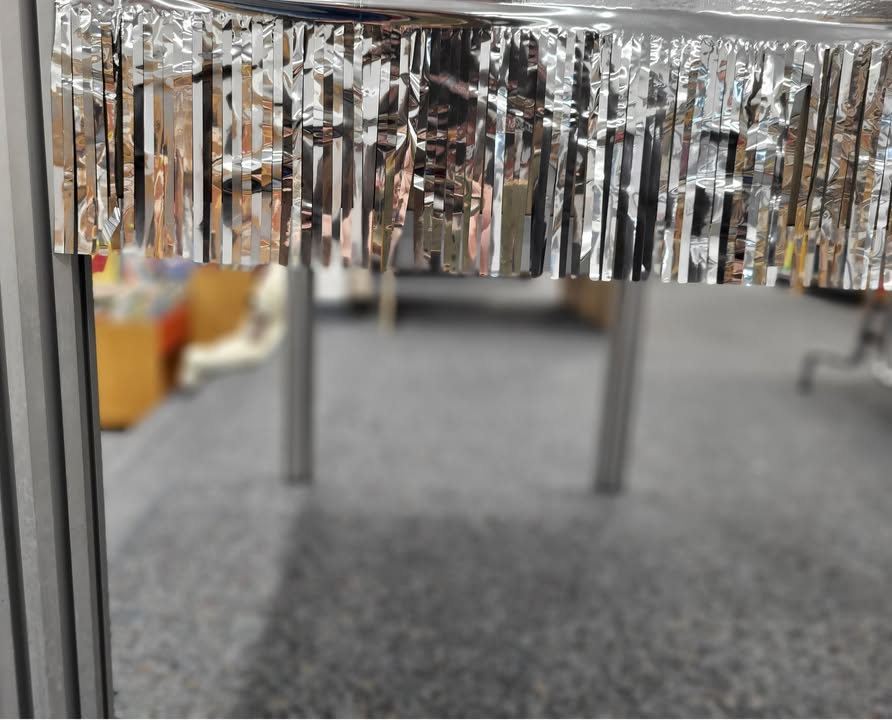 Dieser Alternativtext wurde KI-generiert: Eine metallische Folienvorhangdekoration hängt vor einem verschwommenen Hintergrund. Das Bild ist farbig und zeigt eine Innenraumansicht.