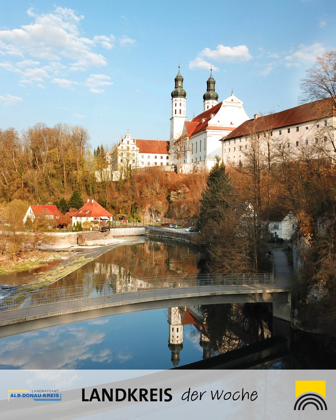 Dieser Alternativtext wurde KI-generiert: Ein farbiges Bild zeigt eine historische Gebäudeanlage mit Türmen und roten Dächern an einem Fluss. Im Hintergrund sind Bäume und ein klarer Himmel zu sehen.